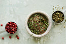 Three measuring cups—one filled with red berries, another with green dried herbs, and a third with greenish dried seeds or small herbs—are artfully arranged on a light textured surface, highlighting the World Spice Emerald City Seasoning by World Spice and celebrating the diverse local ingredients and Pacific Northwest flavors it brings to your kitchen.