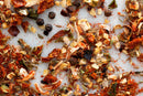 A close-up of assorted dried spices and herbs scattered on a white surface, featuring pieces of garlic, crushed red pepper, black peppercorns, paprika, and a touch of World Spice Fajita & Taco Spice by World Spice—ideal for crafting full-flavored fajitas or seasoning your favorite ground meat dishes.