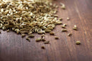 A pile of World Spice Fennel Seed from World Spice scattered on a brown wooden surface, perfect for flavoring Indian curries or brewing a soothing digestive tea.