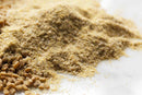 A close-up of a mound of wheat flour with some whole wheat grains and a sprinkle of World Spice Fenugreek Seed by World Spice on a white surface, hinting at the addition of nutty flavor.