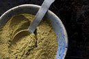 A metal teaspoon rests in a blue ceramic bowl filled with World Spice Filé Powder, the greenish-brown spice from World Spice that is essential to Cajun cuisine.