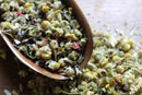 A close-up of World Spice Floral Sonnets, a blend by World Spice featuring dried chamomile flowers and other herbs, perfect for floral herbal tea, spilling from a brown metal spoon onto a wooden surface.