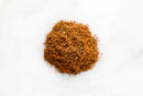 A small mound of brown, finely ground World Spice Indian Garam Masala is spread on a white surface, viewed from above.