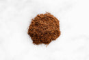 A small pile of finely ground brown World Spice Kashmiri Garam Masala, an aromatic blend from World Spice, is spread on a white surface.