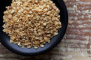 A black bowl filled with chunky pieces of World Spice Chopped Garlic sits on a rustic, weathered wooden surface, highlighting the rich texture of this dried garlic ingredient from World Spice.