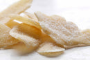 Close-up of several pieces of World Spice Candied Ginger by World Spice, coated with sugar, displayed on a white surface. These light yellow, slightly translucent ginger pieces have a rough texture—perfect for enjoying as a sweet treat on their own or for adding a zesty kick to baked goods like ginger snaps.