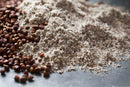 A close-up of whole buckwheat seeds and a pile of finely ground buckwheat flour on a gray surface, capturing the earthy allure reminiscent of World Spice Grains of Paradise by World Spice.