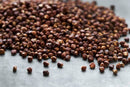 A pile of World Spice Grains of Paradise, scattered on a gray surface, evokes the rich allure of exotic spices.