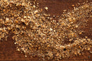 A close-up of a scattered pile of World Spice Habanero Garlic Pepper—a blend of mixed ground nuts, kosher salt, spices, and Vietnamese black pepper—on a dark wooden surface.