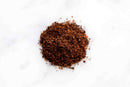 A small pile of finely ground, dark brown World Spice Harissa—a North African spice blend from World Spice—sits on a white background.