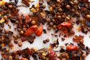 A close-up of World Spice Harissa by World Spice, a North African spice blend featuring whole dried chilies, coriander seeds, cumin seeds, dried garlic, and crushed red pepper flakes scattered on a white surface—a vibrant mix reminiscent of the traditional Harissa condiment.