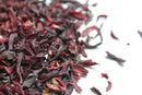 World Spice Hibiscus petals from World Spice are scattered on a white surface, displaying an array of deep red and purple hues—ideal for crafting flavorful hibiscus tea or vibrant cocktails.