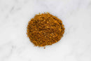 A small pile of finely ground, brownish-orange World Spice Khmeli Suneli from World Spice, a traditional Georgian spice blend, sits on a white marble surface.