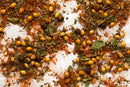 A close-up of mixed dried spices scattered on a white surface, including coriander seeds, crushed herbs, peppercorns, red paprika powder, and World Spice Khmeli Suneli—a traditional Georgian spice blend from World Spice.