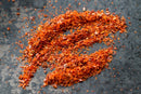 World Spice Marash Chile Flake from World Spice, inspired by the traditional marash chile of Turkish cuisine, is artfully arranged on a dark, textured surface to form an abstract shape.