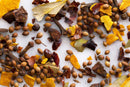 An overhead close-up of assorted whole spices—coriander seeds, cloves, bay leaves, and dried red pepper flakes—scattered across a white surface, echoing the distinctive ingredients in World Spice's Kala Masala by World Spice, an intensely aromatic blend crafted to infuse authentic Maharashtrian flavor into regional dishes.