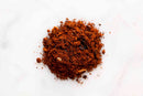 A small pile of World Spice Mole Olé, a reddish-brown and crumbly mole powder from World Spice, is scattered on a white surface.