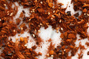 Close-up of World Spice Mole Olé by World Spice, a classic Mexican seasoning blend of crushed red pepper flakes and seeds, scattered on a white marble surface.