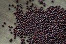 A close-up of many small, round, dark brown World Spice Brown Mustard Seeds—sometimes called mustard caviar—scattered on a wooden surface.