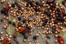 A vibrant blend of whole dried spices—including coriander seeds, bay leaves, peppercorns, dried red chilies, and allspice—from World Spice Pickling Spice by World Spice, scattered on a wooden surface; ideal for pickling or crafting a classic British condiment.