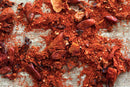 World Spice Piri Piri Blend by World Spice, featuring a mix of crushed red chili peppers—including fiery African chiles—scattered on a light gray surface, highlights its blend of both powdery and chunky textures.