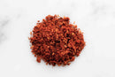 A vibrant scatter of World Spice Piri Piri Blend—a signature mix from World Spice featuring fiery African chiles and aromatic spices—creates a striking reddish-brown display on a white surface, capturing the bold heat and lively character of this classic seasoning.