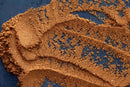 Brown sugar is scattered and smeared across a dark blue surface, mingling with traces of World Spice Pumpkin Pie Spice by World Spice to create textured patterns and clumps in various areas.