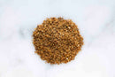 A small pile of World Spice Seattle Salmon Rub by World Spice, finely ground with a rich brown hue and subtle notes of roasted spices, sits on a white marble surface.