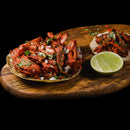 Two tacos filled with seasoned shredded meat, chopped onions, and cilantro—perfectly enhanced with a dash of The Spice Lab Ground Cumin 1 lb Bulk Foodservice Spice—sit on a wooden board next to a halved lime, all against a black background.