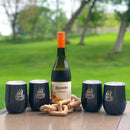 A bottle of Riunite Sangria sits on an outdoor table, surrounded by four black WPPO WPPO Hot and Cold Tumblers With Lid from WPPO LLC Direct—each featuring the “WPPO Get Fired Up” logo and vacuum insulation—alongside a decorative wooden chain. Lush green trees and grass create a vibrant backdrop.