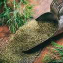 A metal scoop filled with The Spice Lab Organic Whole Dill Weed rests on a wooden surface, surrounded by fresh sprigs—perfect for adding a burst of flavor to homemade tzatziki.