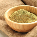 A wooden bowl filled with The Spice Lab Ground Oregano rests on a burlap fabric surface.