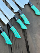 Six large Texan Knives from the Stainless Knife Set feature 13" forged stainless steel blades and turquoise-gold epoxy resin handles, displayed side by side on a rustic wooden surface with blades facing up.