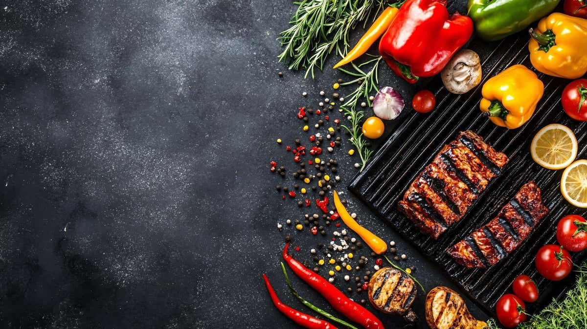 Grilled meat and vegetables, including bell peppers, tomatoes, eggplant, mushrooms, and lemon slices, arranged on a dark surface with herbs and colorful peppercorns.