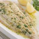 A cooked fillet of fish garnished with The Spice Lab Organic Parsley Flakes and sauce, served on a white plate with lemon wedges in the background.