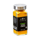 A transparent glass jar with a silver lid contains vibrant yellow organic ground turmeric, ideal for Indian cuisine. The black label displays “The Spice Lab Organic Ground Turmeric” and the net weight is 2 oz (56g).