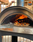A WPPO LLC Direct Karma 25 Colored Wood-Fired Oven With Stand/Cart is shown with a pizza baking inside, ideal for outdoor cooking. Bright flames flicker at the back of the stainless steel wood-fired oven, emphasizing its power, while the WPPO logo appears in the upper right corner of the image.