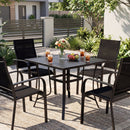 A modern patio features the DirectDeals 5 Pieces Patio Dining Set for 4 Outdoor Square Table and Stackable Chairs, with stylish black metal, surrounded by greenery and modern fencing.