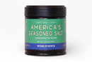 A 3.53 oz (100g) jar of World Spice America's Seasoned Salt, featuring a green label with white text and descriptors such as umami, salty, and smoky. This handcrafted blend by World Spice combines Italian sea salt and smoky paprika for a bold, flavorful experience, and is labeled "Handcrafted Blend.