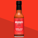 A bottle of Bravado Spice Árbol Chili & Garlic Hot Sauce by Bravado Spice—made with authentic Chiles de Árbol—showcases a red label, black cap, and delivers a medium heat level, all set against a vivid red geometric backdrop. This bold Mexican hot sauce adds vibrant flavor and the perfect touch of heat to any dish.