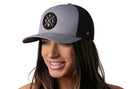 A woman with long brown hair smiles while wearing the Haka Hat Atlanta Trucker Hat | Gray-Black ATL X Snapback, featuring a round ATL logo. The snapback from Haka Hat stands out against the plain white background.