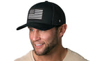 A man wearing a light tan t-shirt and a Haka Hat American Flag Trucker Hat—Black USA Monochrome Snapback.
