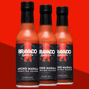Three bottles of Bravado Spice Ancho Masala Scorpion-Reaper Hot Sauce by Bravado Spice, each with a black cap, are arranged together against a vivid red background. The label reads “Super Hot” and features a pepper graphic, highlighting this bold Indian Spiced Hot Sauce as the Ancho Masala flavor you’ve been craving.