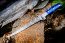 The Texan Knives Custom Handmade Angling Knife features a Damascus steel blade and resin handle, shown on a log beside a filleted fish—an eye-catching addition to your 2025 fishing gear.