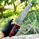 A gloved hand holds the Texan Knives Antique Damascus Steel Bowie Knife – 11" with brass guard and Pakka wood handle outdoors, with green foliage and sunlight in the background.