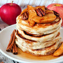 A stack of pancakes topped with caramelized apples, pecans, and syrup is dusted with SALTOPIA Cinnamon Sugar: CRACKLIN' HEIGHTS 16oz—an infused cinnamon sugar perfect for baking from SALTOPIA Infused Sea Salts.