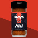 A 2.7 oz bottle of Bravado Spice Co Garlic & Árbol Seasoning, a bold Tex-Mex blend by Bravado Spice Co, featuring a striking black label and showcased on a red geometric background—perfect for adding vibrant flavor to brisket and your favorite dishes.