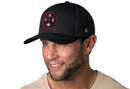 A smiling man with a short beard and mustache wears a Haka Hat Arizona Trucker Hat—Black PHX X Football Snapback, featuring a circular red and white PHX patch—along with a light shirt, in front of a white background.