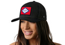 A woman smiles against a white background wearing the Haka Hat Arkansas Flag Trucker Hat, a black snapback by Haka Hat featuring a red, white, and blue state flag patch on the front.