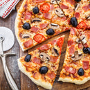 A freshly baked pizza with black olives, mushrooms, tomato slices, and ham sits on a wooden board. One slice is pulled out. The aroma is enhanced by SALTOPIA Infused Sea Salts’ Tomato & Italian Herbs Seasoning: MYSTICAL PIZZA.